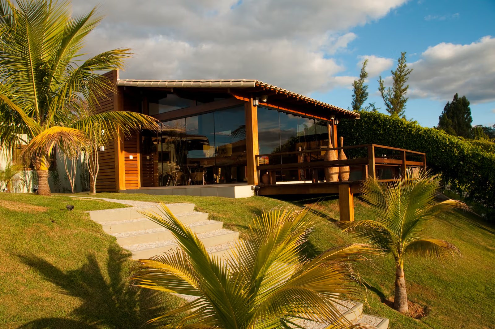 Casa em madeira e vidro ao entardecer, com varanda ampla e jardim