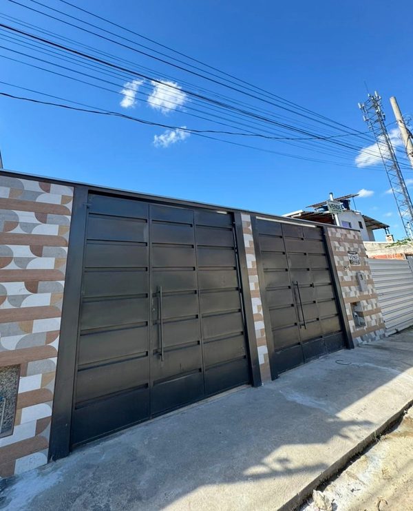 Fachada da casa geminada, com portão de garagem em chapa preta e muro revestido