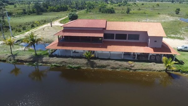 Vista aérea da sede de telhado alaranjado à beira de uma das lagoas, cercada por gramado e coqueiros