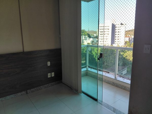 Sala com piso claro e varanda envidraçada, com vista para prédios e morros ao fundo