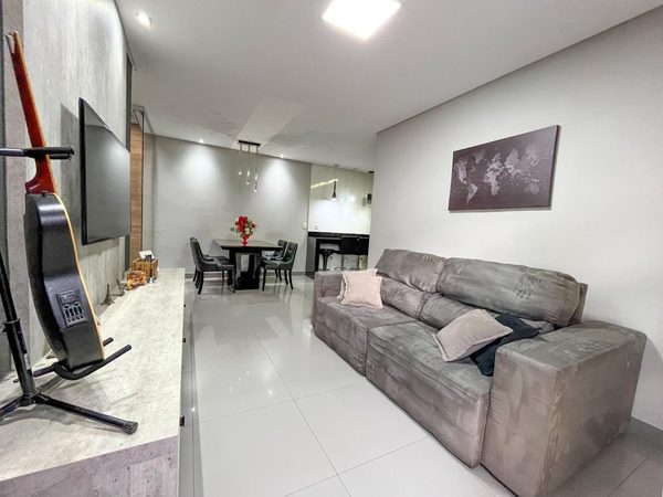 Sala de estar integrada à sala de jantar, com painel de TV, sofá cinza e iluminação embutida