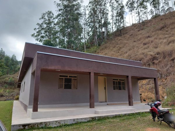 Casa térrea com varanda ampla, cercada por gramado e mata de eucaliptos na encosta
